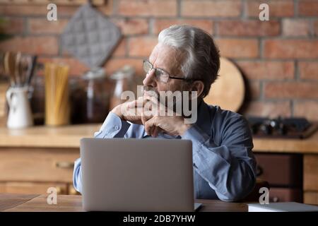 Thoughtful mature man wearing glasses using laptop, looking to aside Stock Photo