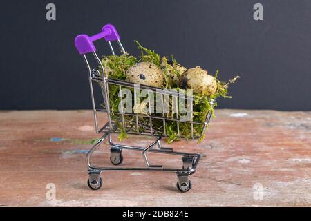 Quail eggs stand in a basket of supermarket filled with moss stand on a wooden table. Top views. Stock Photo