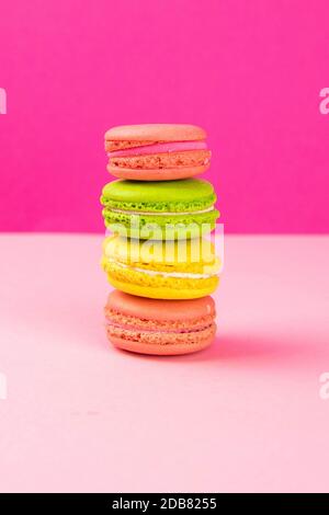 Multi-colored macaroons stand in a pile on a pink table. Close-up Stock Photo
