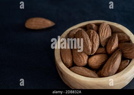 Almonds in a wooden bowl on a black table. Close-up and minimalist shot. top view Stock Photo