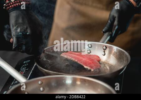 Two frying pans with tuna steak on induction stove Stock Photo