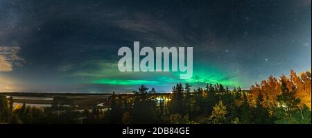 Scenic Aurora Borealis panorama photo across the whole horizon, above autumn birch and pine tree forest, city lights in Swedish countryside close to U Stock Photo