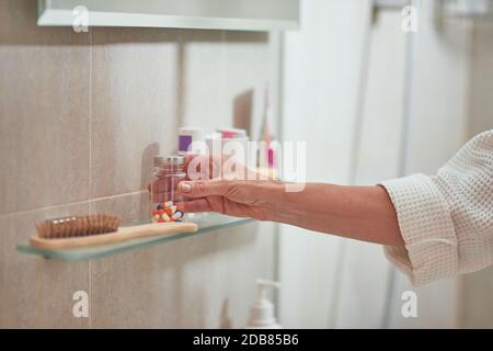 Wellness vitamins bottle on shelf in bathroom held by woman hand. Beauty and cosmetology concept Stock Photo