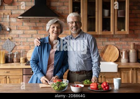 Portrait happy mature family hugging, standing in kitchen, cooking together Stock Photo