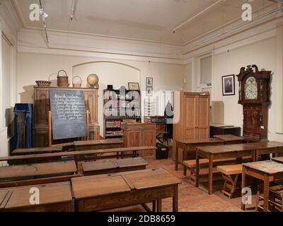 Museum school room desks blackboard tall clock book shelves seats wood cupboard wood floor Stock Photo