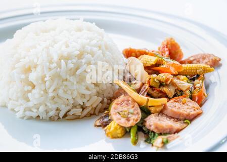 Asian spicy hot food or Thai food, closeup side view Thai sour pork or Nham fried with pepper and mixed vegetable with white cooked rice on round whit Stock Photo
