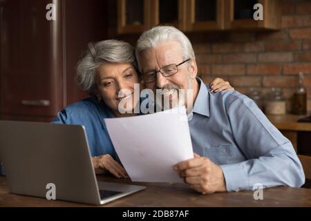 Smiling mature couple reading letter with good news, using laptop Stock Photo