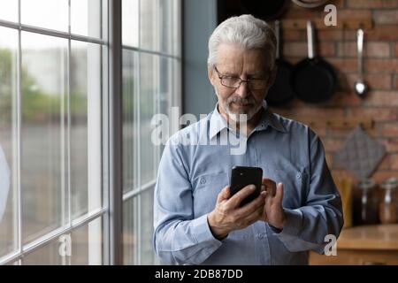 Close up satisfied mature man wearing glasses using phone Stock Photo
