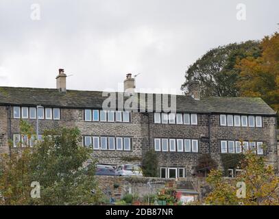 Row of four three story stone built weavers cottages with rows of small windows on top two floors stone roof and chimney pots Stock Photo