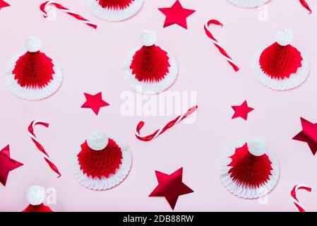 Creative minimal christmas pattern background. Christmas candy canes, red stars and paper santa caps on a pink background. New Year layout concept Stock Photo