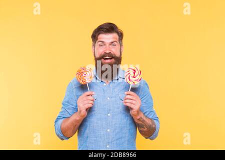Happy bearded man hold tasty rainbow swirl candy pops great for birthday party and candy buffet yellow background, celebration. Stock Photo