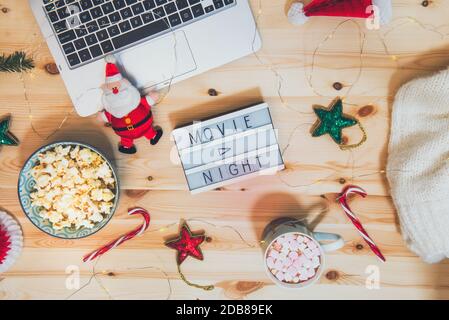 Top view Christmas Movie night concept. Flat lay composition with Movie night message on the board, laptop, popcorn bowl, decor, a cup of cocoa with Stock Photo