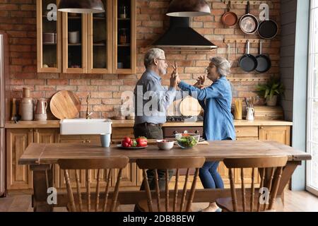 Happy mature married couple dancing in kitchen, enjoying leisure time Stock Photo