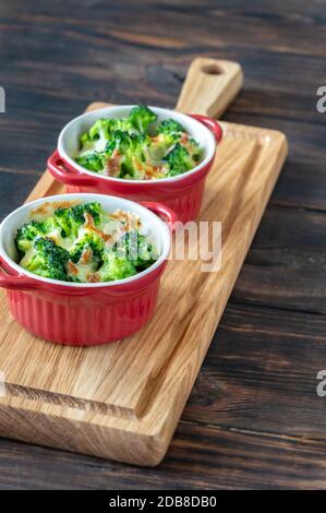 Two pots with baked broccoli and cheese on wooden board Stock Photo
