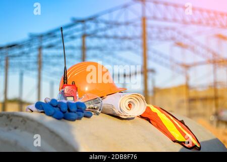 Reflective clothing, hard hat, gloves, walkie-talkie and construction plans on a building site, Thailand Stock Photo