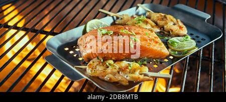 Fresh seafood for grilling over a barbecue with prawn kebabs and salmon steak ready seasoned wt herbs on a roasting pan Stock Photo
