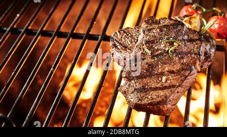 Two portions of thick tender seasoned grilled beef steak on a BBQ grill keeping warm over the hot coals in a panorama banner with copy space Stock Photo