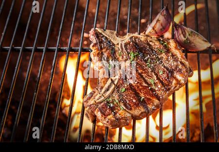 Bone-in rib eye steak seasoned with herbs and spices grilling ver a hot BBQ fire in a view from above with copy space Stock Photo