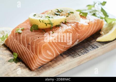 Close up on a thick raw fillet of salmon seasoned with fresh herbs and lemon ready for grilling on a wooden cutting board Stock Photo