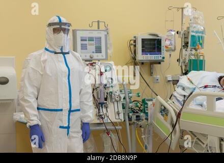 Male nurse with protective coverall clothing in intensive care unit in hospital.  Dialysis machine, to which patient is connected.  The patient fell i Stock Photo