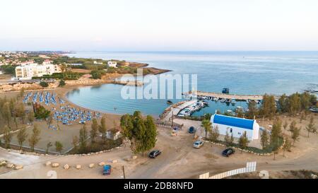 Aerial view of coastline sunset and landmark white washed chapel at Agia Triada beach, Protaras, Famagusta, Cyprus from above. Bird's eye view of tour Stock Photo