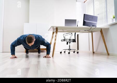 Businessman Doing Push Up On Hardwood Floor In Office Stock Photo