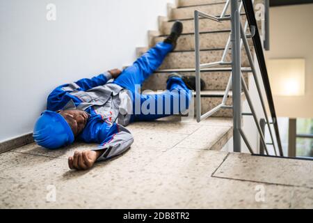 Unconscious Handyman Lying On Staircase With Helmet On Floor Stock Photo