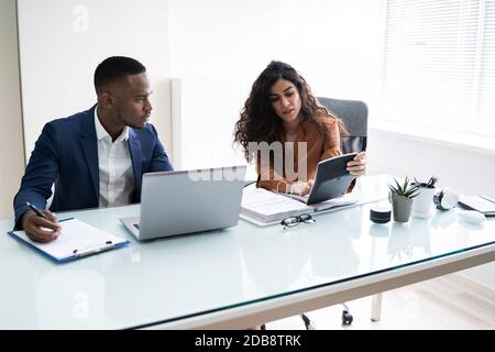 Two Young Businesspeople Calculating Invoice With Calculator Stock Photo