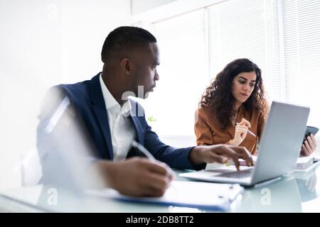 Two Young Businesspeople Calculating Invoice With Calculator Stock Photo