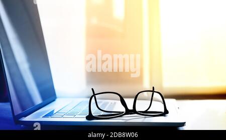 open laptop on which lie reading glasses in black frames Stock Photo