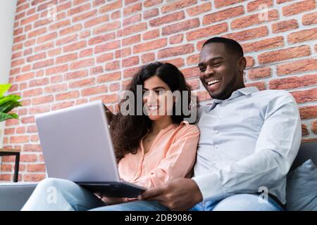 Portrait Of A Happy Young Couple Sitting On Couch Using Laptop Stock Photo