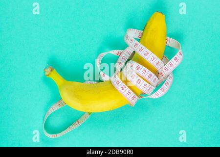 Banana with tape for measuring figure. Centimeter ruler spinned around fruit. Tape wrapped around banana isolated on mint background. Weight loss, hea Stock Photo