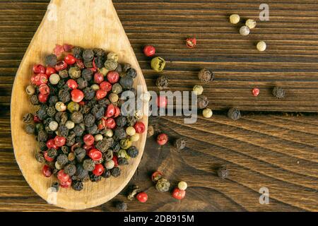 Multi-colored pepper on a wooden spoon and sprinkled side by side on a wooden table. Top views with clear space. Stock Photo