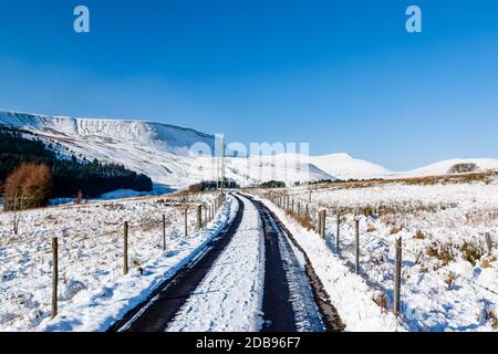 A narrow road leading to snow covered mountains on a bright, sunny day in winter Stock Photo