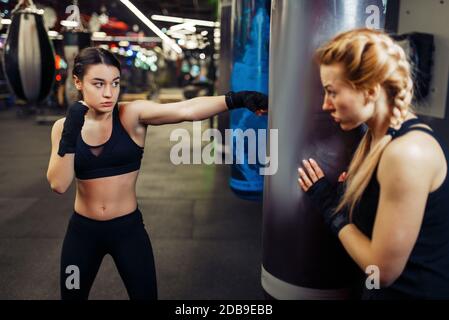 Woman in boxing bandages hits a punching bag, box training with trainer. Female boxers in gym, kickboxing workout in sport club, punches practice Stock Photo