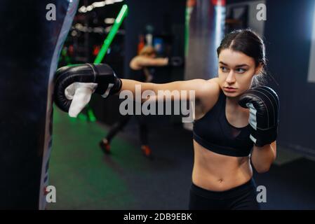 Woman in black boxing bandages and sportswear hits a punching bag, box training. Female boxer in gym, girl kickboxer in sport club, punches practice Stock Photo