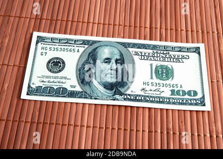 A hundred American dollars bill in close-up on a bambuk mat made of thin brown bamboo sticks. Located slightly on the diagonal. Stock Photo