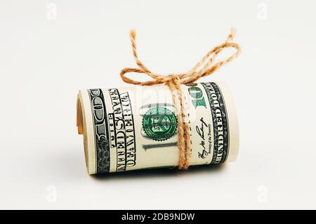 Isolated roll of dollars. A large roll of hundred-dollar bills lies on a white background in the middle of the image, tied with a rope. Close up. Full Stock Photo