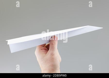 A hand holding a paper dart plane ready to throw Stock Photo