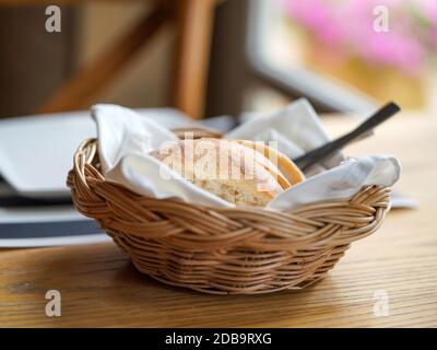 French bread sliced in a basket on a wooden table near the window. Stock Photo