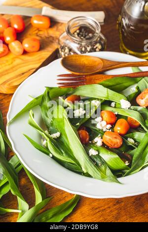 Fresh salad with wild garlic,tomatoes and feta cheese on plate. Ramsons leaves. Stock Photo