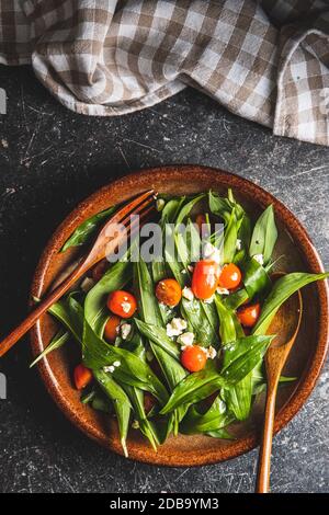 Fresh salad with wild garlic,tomatoes and feta cheese on plate. Ramsons leaves. Top view. Stock Photo