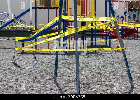 A single swing is caution taped off on a playground swing set during COVID-19 pandemic. Stock Photo