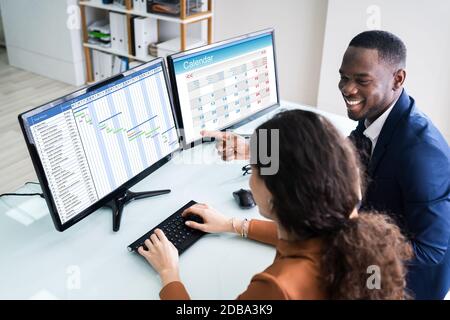Young Businesspeople Analyzing Gantt Chart And Calendar On Computer In Office Stock Photo