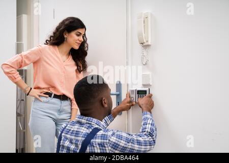 Close-up Of Handyman Installing Security System Near Door Wall While Woman Using Remote Stock Photo