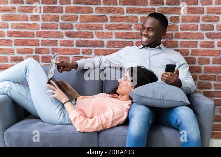 Couple Using Laptops While Relaxing On Sofa At Home Stock Photo