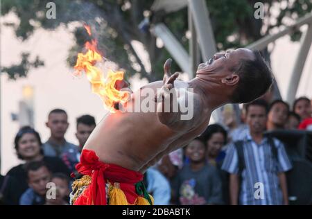 A performer rolling fire sticks on his body as the crowd watches Stock Photo