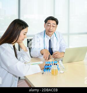 Couple of Asian adult  male doctor and Asian young female doctor wearing formal white coat teamwork brainstorm meeting with computer laptop at the hos Stock Photo