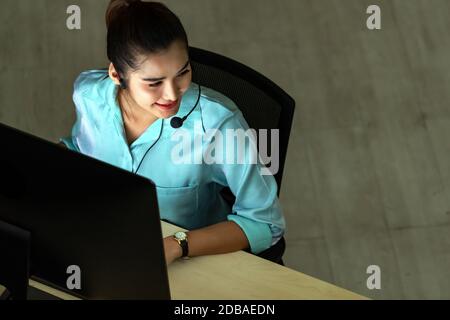 Late Night Environment. Top view of young adult friendly operator call center girl woman with headsets working hard at night. Using for 24 Hr. 7 days Stock Photo