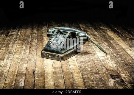 black retro telephone with a rotary dial stands on a wooden floor in the dark Stock Photo